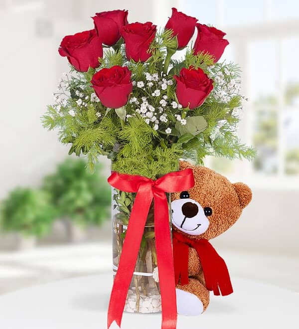 Seven red roses in a vase, teddy bear.